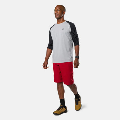 Man wearing a gray and black long-sleeve shirt with red shorts on a white background