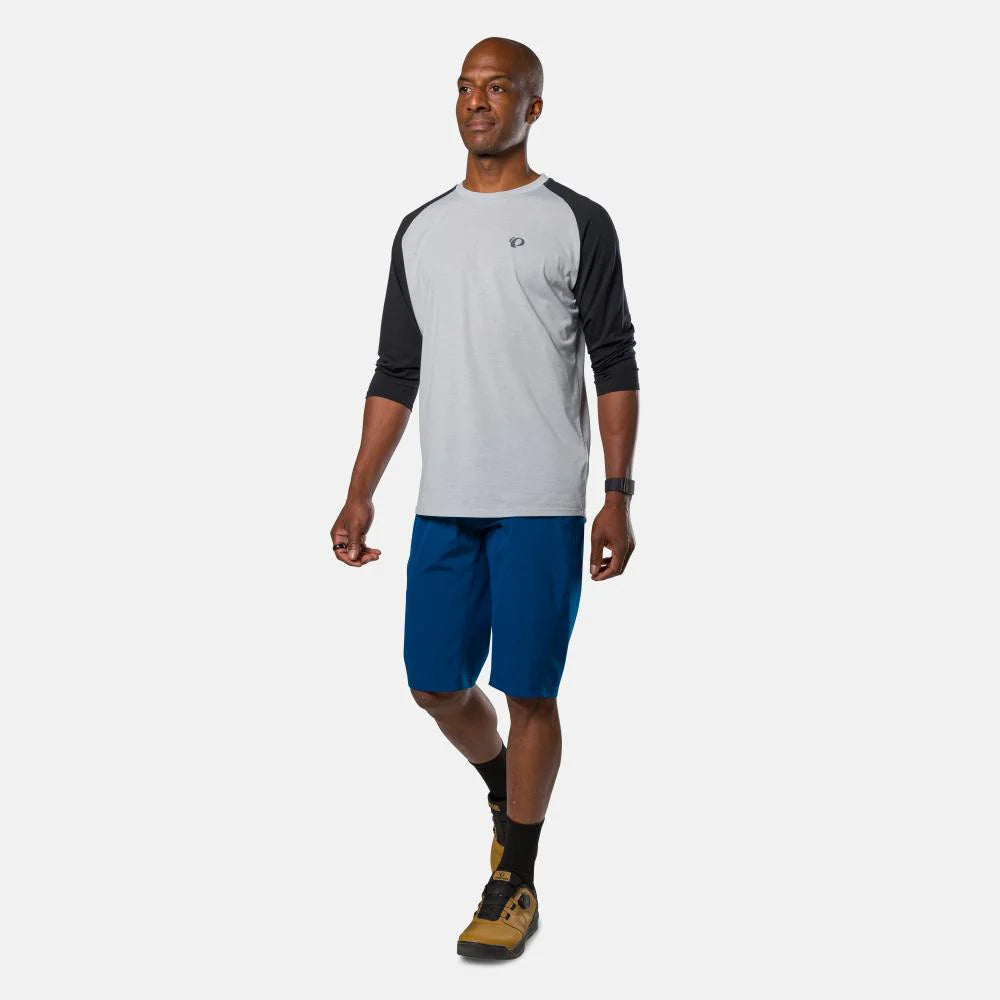Man wearing a gray and black long-sleeve shirt with blue shorts on a white background