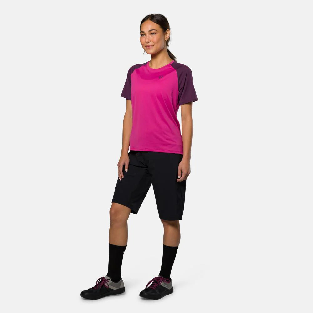 Woman wearing a pink and purple athletic shirt with black shorts on a white background