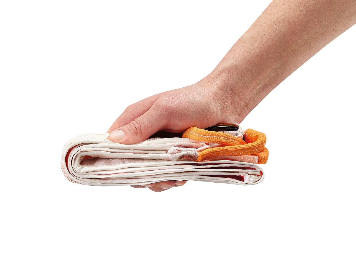 Hand holding a stack of folded clothes with orange garment tags on a white background