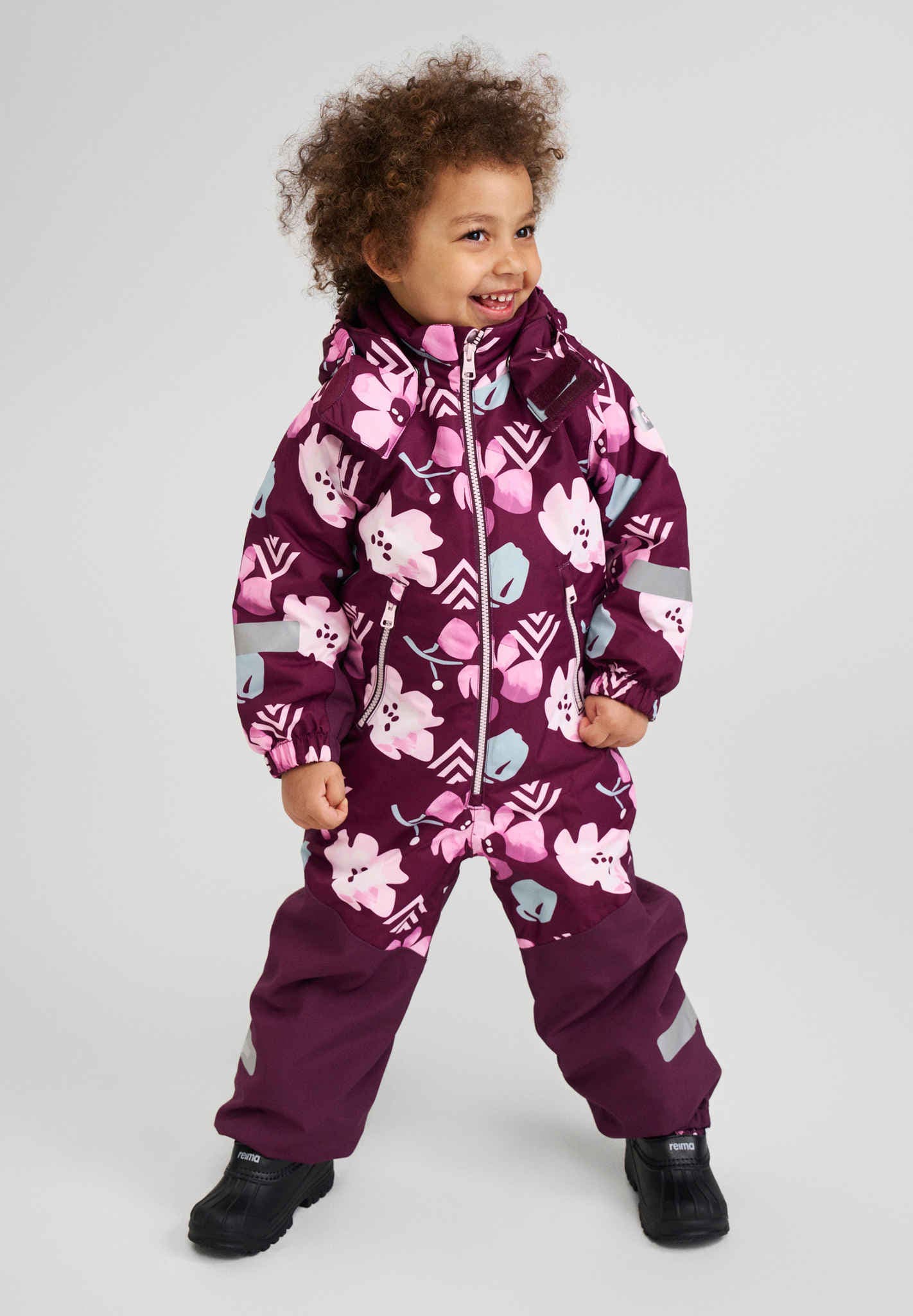 Child wearing a purple snowsuit with floral patterns on a light gray background