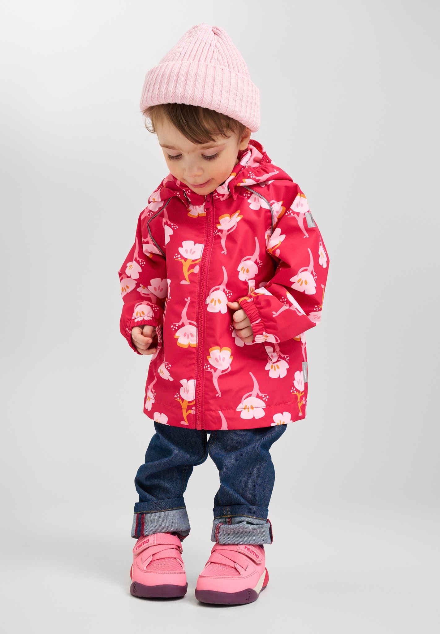 Child wearing a red floral coat, pink boots, and a pink hat on a light gray background