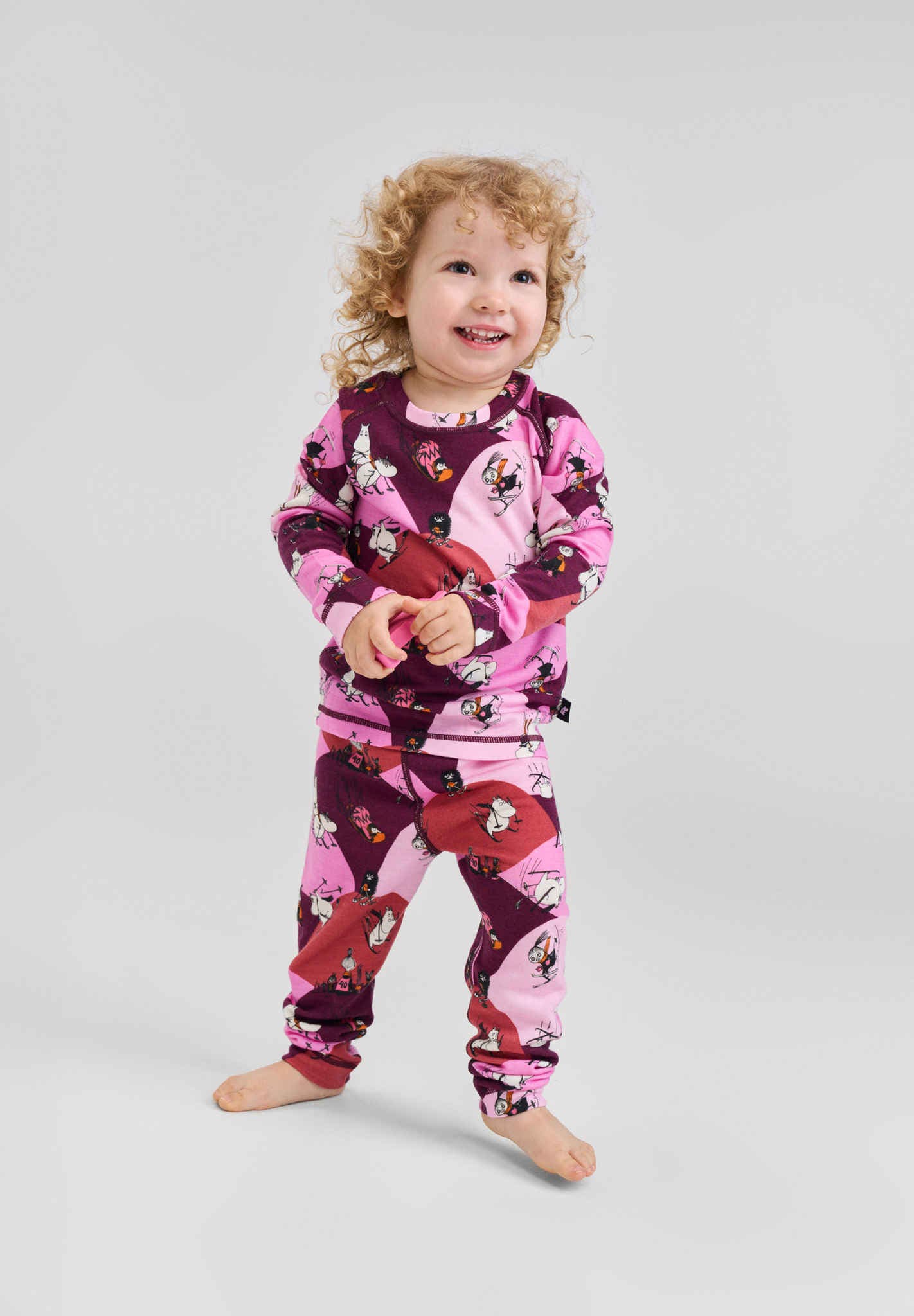 Child wearing a pink and purple pajama set with cartoon characters on a gray background