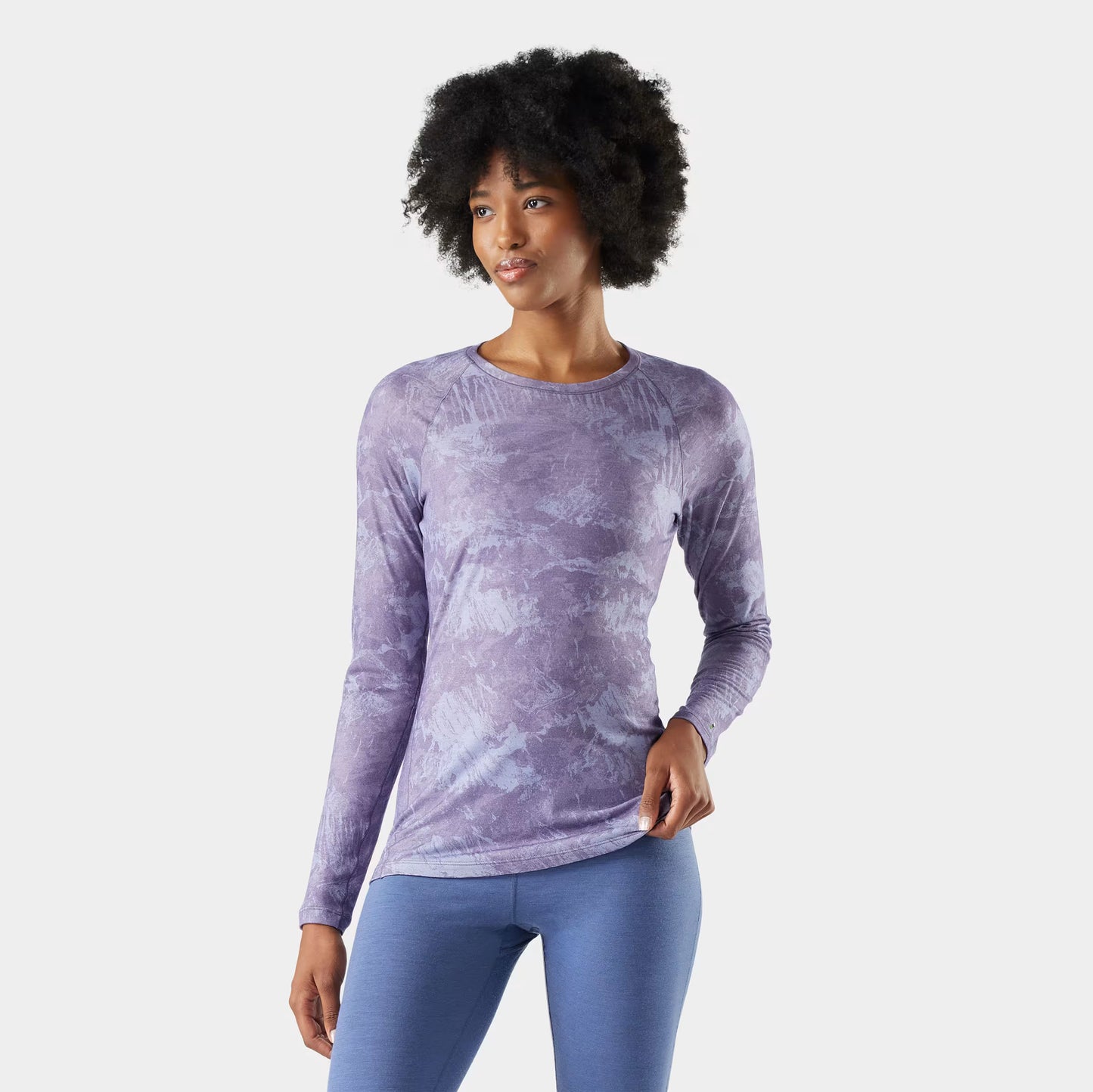 Woman wearing a purple tie-dye long-sleeve top and blue leggings on a light gray background