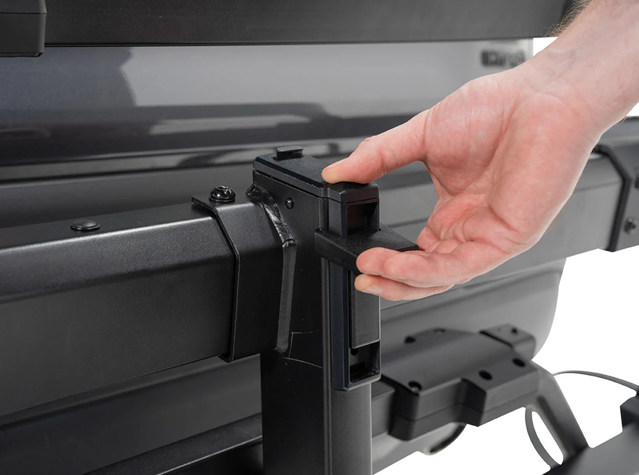 Hand interacting with a black metal bracket on a vehicle's roof rack.